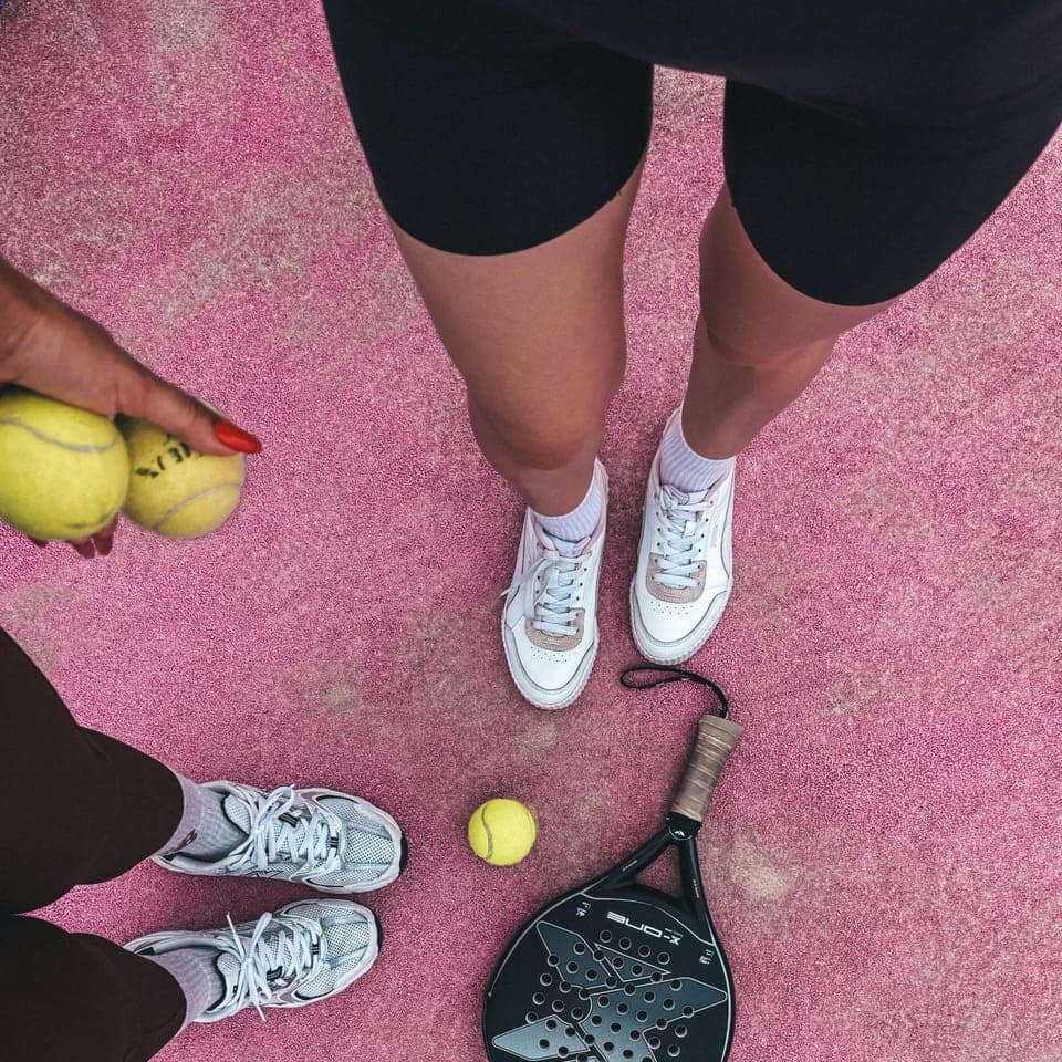 Två par fötter och padelracketar på en bana ovanifrån