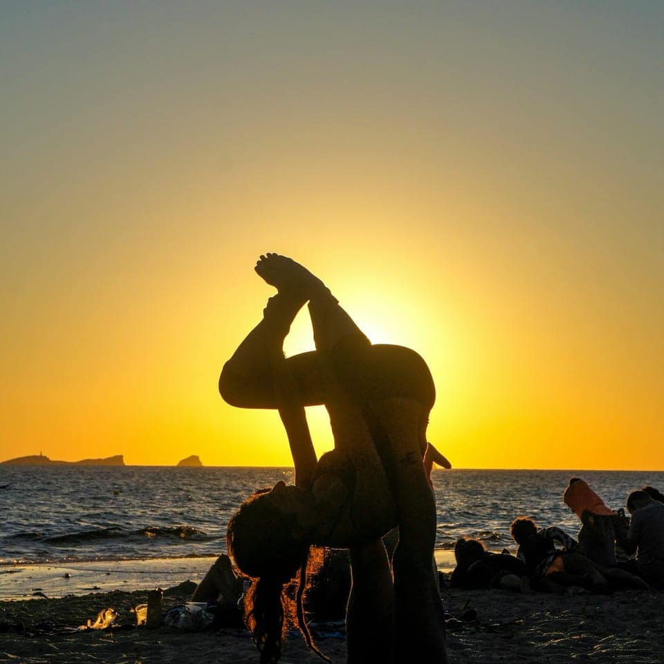 Silhuetter som gör acro-yoga på en strand vid solnedgång