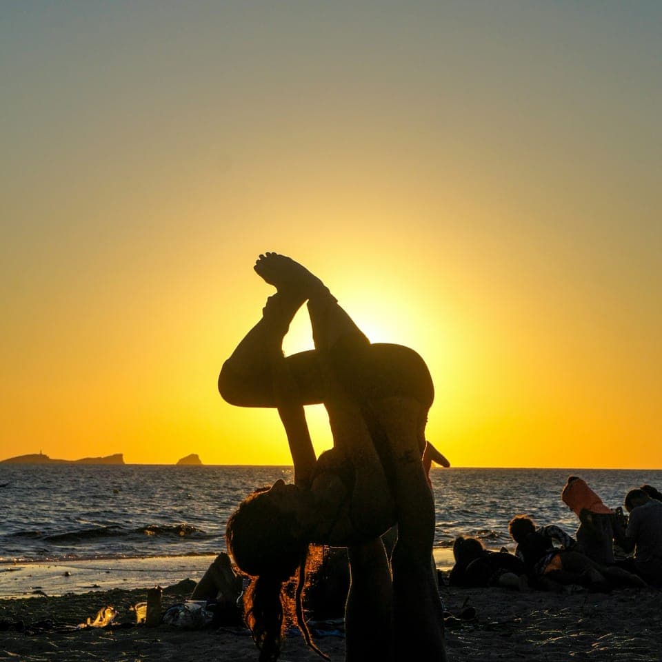 Silhuetter som gör acro-yoga på en strand vid solnedgång